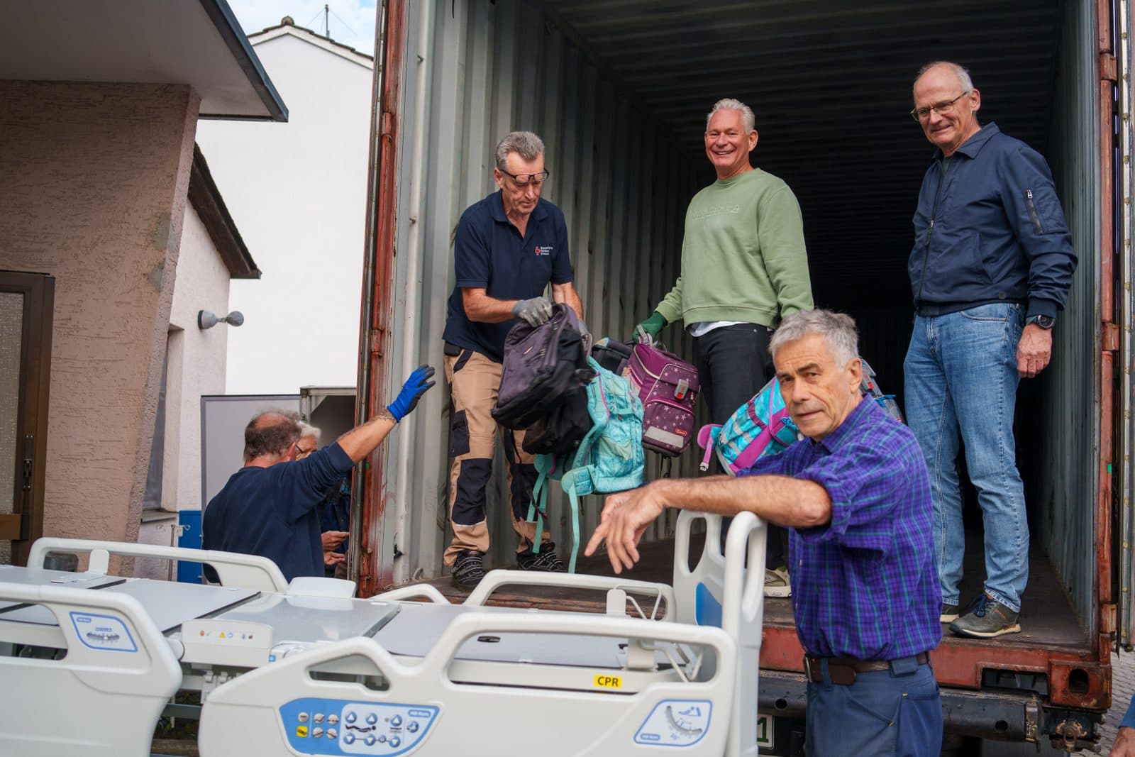Mehrere Personen beladen einen Container mit Schulranzen.
