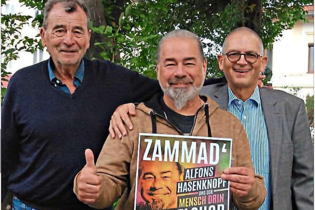 3 Personen halten ein Veranstaltungsplakat.